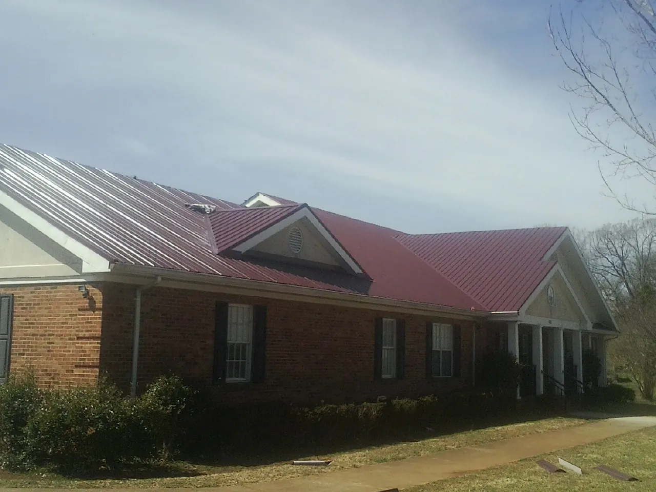 Red metal roof with gabled entries on a long brick building, from a Hail Damage Roof Repair job in Sheldon