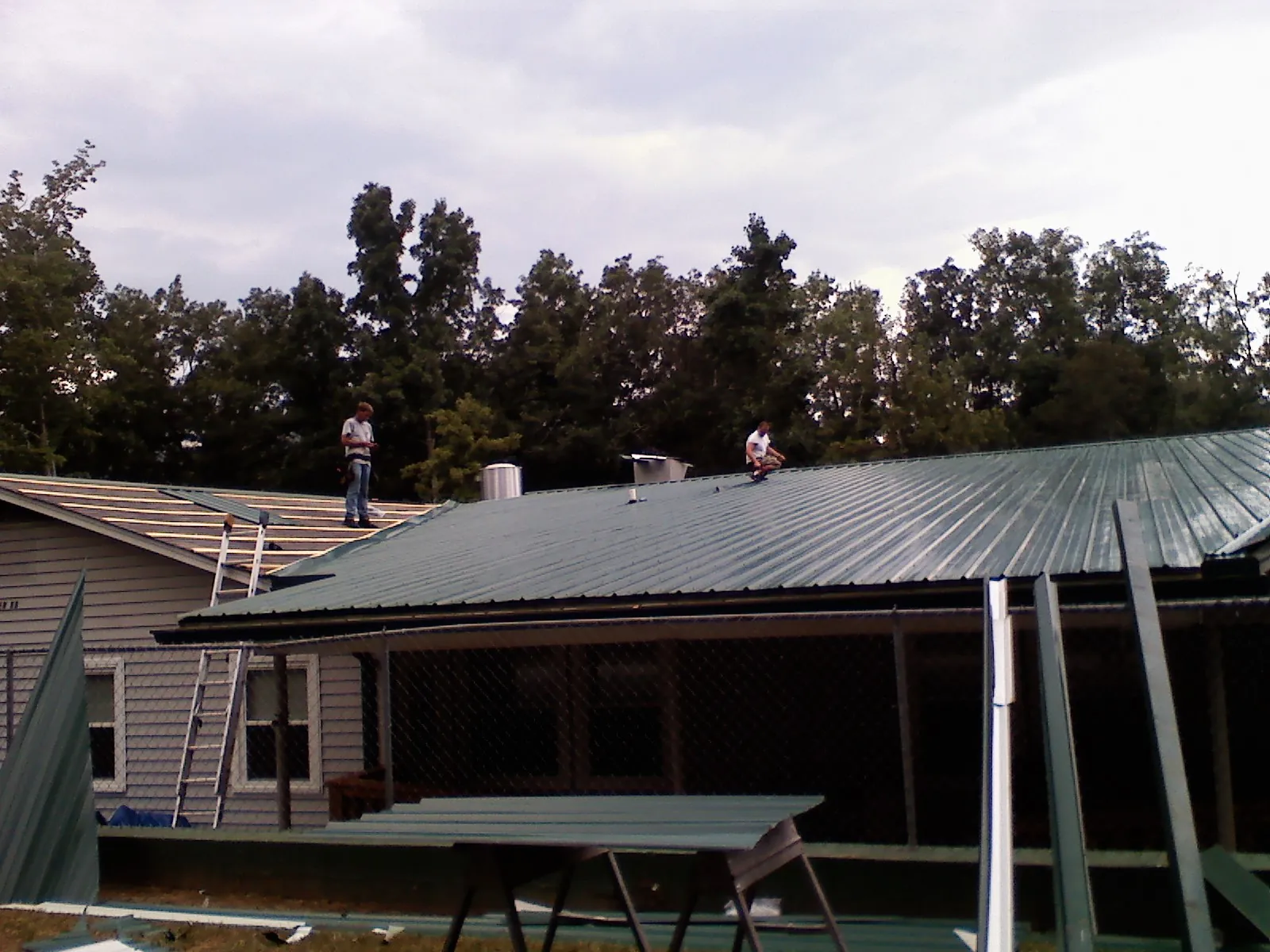 Two roofers installing green metal panels above a covered porch in Sheldon